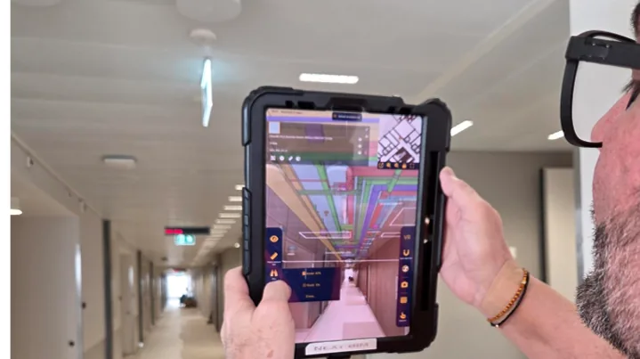 Mitarbeiter nutzt Tablet mit NEXT-BIM Augmented Reality im Korridor des Kantonsspitals Aarau, BIM-Modell zeigt verdeckte Leitungen &uuml;ber der Decke